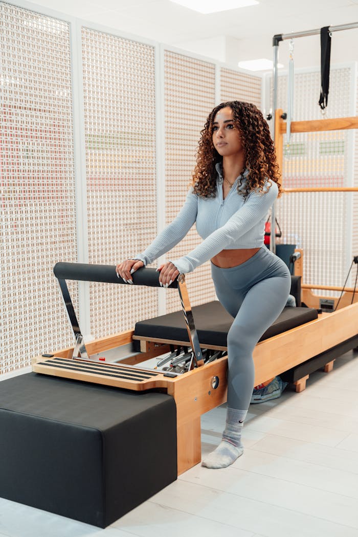 Woman exercising on pilates reformer machine indoors. Focus on fitness and wellbeing.